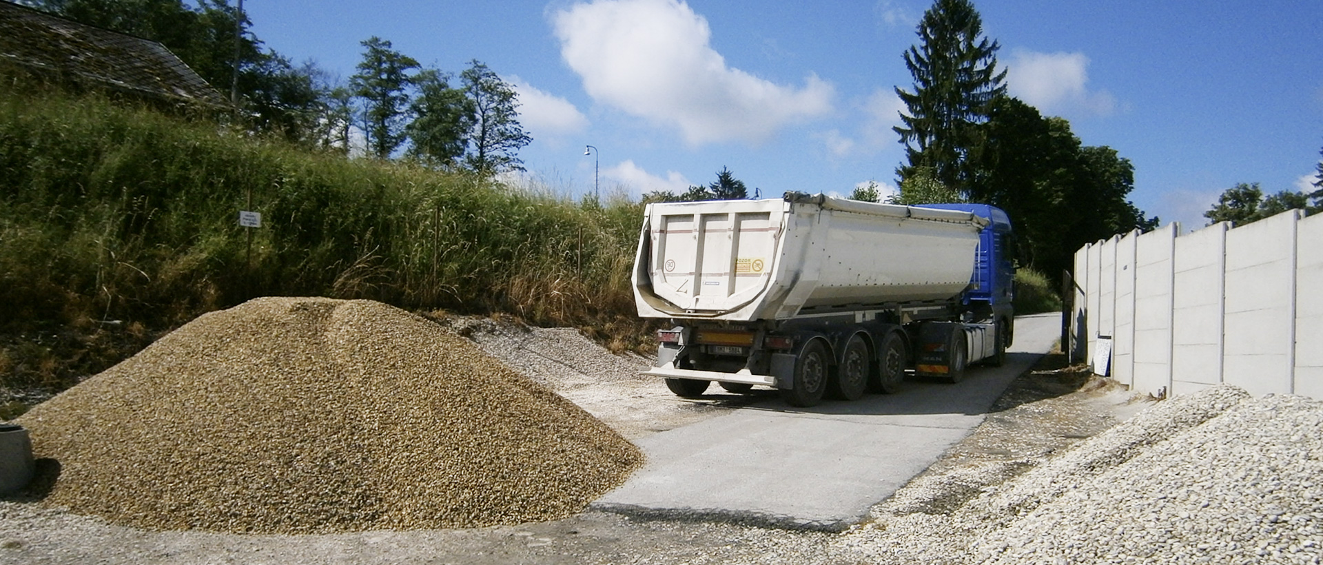 Sypký stavební materiál a sklápěcí souprava v areálu